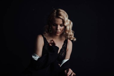 Young adult beauty woman in formal evening suit of black color with lace bra at thoughtful. Stylish blonde curly hair sensual model fashionista posing at studio in fashion pantsuit