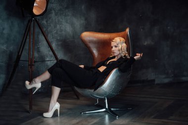 Young adult beauty woman in formal evening suit of black color with lace bra at thoughtful. Stylish blonde curly hair sensual model fashionista posing at studio in fashion pantsuit