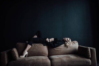 Young adult beauty woman in formal evening suit of black color with lace bra at thoughtful. Stylish blonde curly hair sensual model fashionista posing at studio in fashion pantsuit