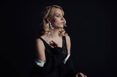 Young adult beauty woman in formal evening suit of black color with lace bra at thoughtful. Stylish blonde curly hair sensual model fashionista posing at studio in fashion pantsuit