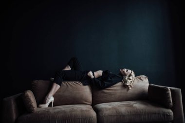 Young adult beauty woman in formal evening suit of black color with lace bra at thoughtful. Stylish blonde curly hair sensual model fashionista posing at studio in fashion pantsuit