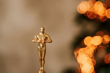 Hollywood gold oscars trophy figurine imitation seen during an award cinema ceremony. Success and victory concept close up statuette at twinkle yellow lights background