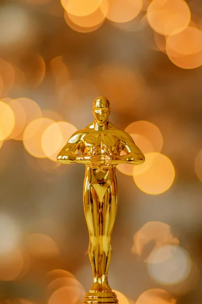 Hollywood gold oscars trophy figurine imitation seen during an award cinema ceremony. Success and victory concept close up statuette at twinkle yellow lights background