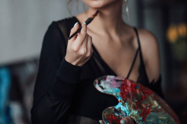 Yetişkin, zarif, siyah bluzlu genç bir kadın. Havalı, kıvırcık saçlı, şehvetli model, çıplak omuz mankeni, boya paletiyle poz veren, brüt sarılan, stüdyo ressamları.