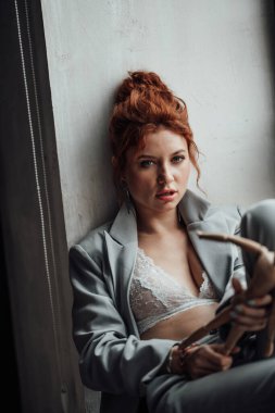 Yetişkin, zarif ve zarif bir kadın resmi akşam gri takımlı, beyaz sütyenli, düşünceli. Havalı, kıvırcık, kıvırcık saçlı, şehvetli model. Moda elbisesiyle stüdyoda poz veren çıplak omuz modamız.
