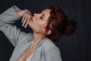 Yetişkin, zarif ve zarif bir kadın resmi akşam gri takımlı, beyaz sütyenli, düşünceli. Havalı, kıvırcık, kıvırcık saçlı, şehvetli model. Moda elbisesiyle stüdyoda poz veren çıplak omuz modamız.