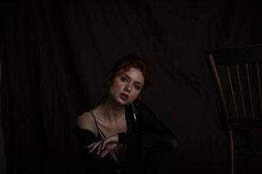 Yetişkin, güzel, zarif bir kadın resmi bir akşam giysisi giymiş, yüzüne siyah bir el değmiş. Havalı, kıvırcık, kıvırcık saçlı, şehvetli model, çıplak omuz modada moda takım elbise ve sutyenle stüdyoda poz veriyor.