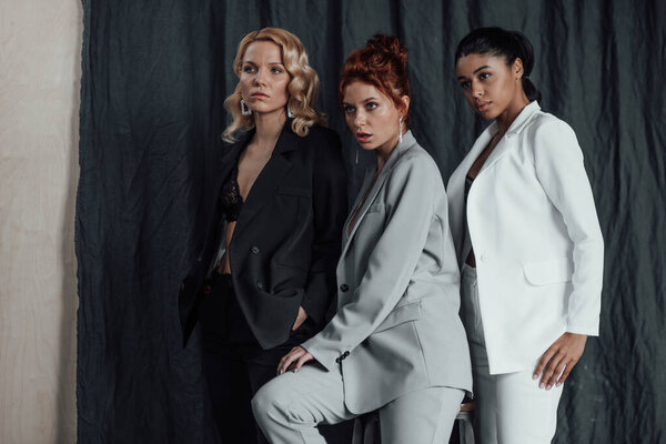 Adult beauty elegant multi ethnic group young girls in formal evening suits of different colors with bra. Stylish diverse people sensual fashionistas posing at studio in fashion pantsuits no shirts