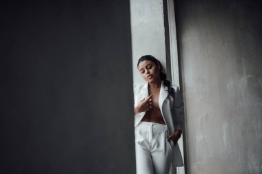 Genç, yetişkin, esmer bir kadın resmi bir gece elbisesi ve düşünceli bir sütyenle. Şık, kıvırcık saçlı, şehvetli, Afro-Amerikan manken modayla stüdyoda moda kıyafeti içinde poz veriyor.