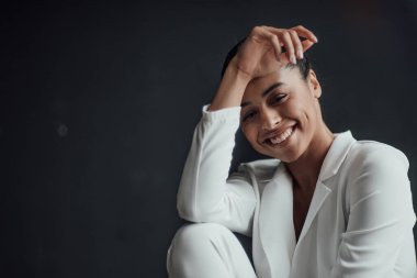 Resmi akşam giysili esmer, genç, güzel bir kadın. Yüzüne tişört değmemiş, beyaz takım elbiseli. Şık, kıvırcık saçlı, şehvetli, Afro-Amerikan manken modayla stüdyoda moda kıyafeti içinde poz veriyor.