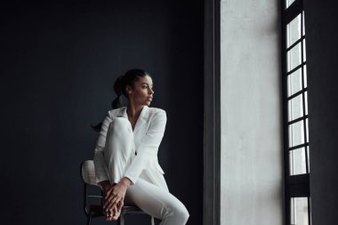 Genç, yetişkin, esmer bir kadın resmi bir gece elbisesi ve düşünceli bir sütyenle. Şık, kıvırcık saçlı, şehvetli, Afro-Amerikan manken modayla stüdyoda moda kıyafeti içinde poz veriyor.