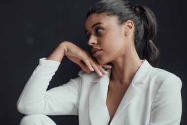 Resmi akşam giysili esmer, genç, güzel bir kadın. Yüzüne tişört değmemiş, beyaz takım elbiseli. Şık, kıvırcık saçlı, şehvetli, Afro-Amerikan manken modayla stüdyoda moda kıyafeti içinde poz veriyor.