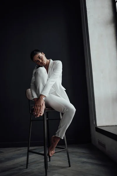 stock image Young adult beauty swarthy woman in formal evening white suit with bra at thoughtful. Stylish black curly hair sensual african american model fashionista posing at studio in fashion pantsuit