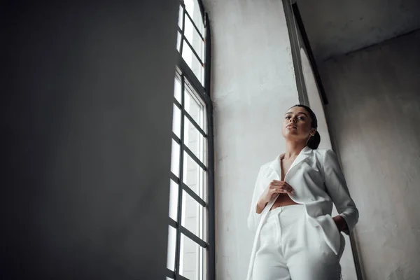 stock image Young adult beauty swarthy woman in formal evening white suit with bra at thoughtful. Stylish black curly hair sensual african american model fashionista posing at studio in fashion pantsuit