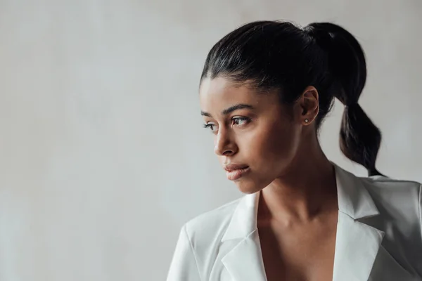 Genç, yetişkin, esmer bir kadın resmi bir gece elbisesi ve düşünceli bir sütyenle. Şık, kıvırcık saçlı, şehvetli, Afro-Amerikan manken modayla stüdyoda moda kıyafeti içinde poz veriyor.
