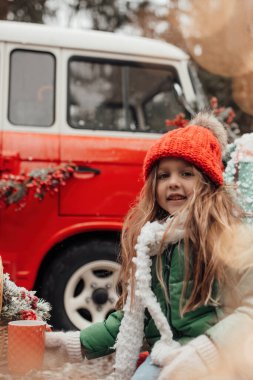 Noel 'i ve yeni yılı kutlayan bayan çocuk kış tatilini dışarıda kutluyor. Kırmızı örülmüş şapkalı küçük bir kız açık havada vakit geçirip Xmas otobüsünün yanındaki büyük bardaktan sıcak çikolata içiyor.