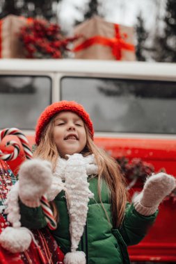 Noel 'i ve yeni yılı kutlayan bayan çocuk kış tatilini dışarıda kutluyor. Kırmızı örgü şapkalı aktif küçük kız elinde Noel şekeri bastonuyla açık havada vakit geçiriyor.