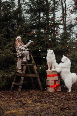 Noel 'i ve yeni yılı kutlayan bayan çocuk kış tatilini dışarıda kutluyor. Küçük kız açık havada beyaz Samoylu köpekle Noel otobüsünün yanında eğleniyor. Çocukluğun tadını çıkarıyor.