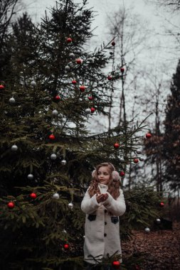 Noel 'i ve yeni yılı kutlayan bayan çocuk kış tatilini dışarıda kutluyor. Aktif küçük kız kozalaklı ormanda çocukluğunun tadını çıkarıyor.