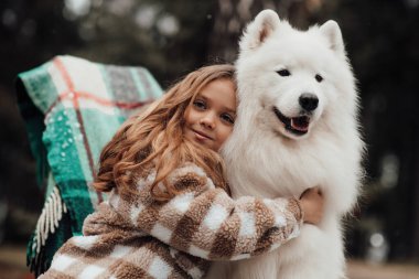 Noel 'i ve yeni yılı kutlayan bayan çocuk kış tatilini dışarıda kutluyor. Küçük kız açık havada beyaz Samoylu köpekle Noel otobüsünün yanında eğleniyor. Çocukluğun tadını çıkarıyor.