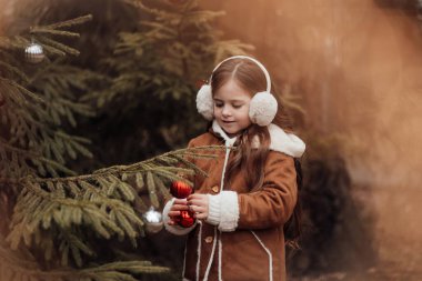 Aktif küçük kız ormanda istirahat edip çocukluk yılbaşı balolarının tadını çıkarıyor. Noel 'i ve yeni yılı kutlayan kadın çocuk kış tatilini dışarıda kutluyor.