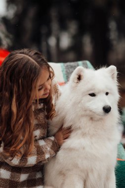 Noel 'i ve yeni yılı kutlayan bayan çocuk kış tatilini dışarıda kutluyor. Küçük kız açık havada beyaz Samoylu köpekle Noel otobüsünün yanında eğleniyor. Çocukluğun tadını çıkarıyor.