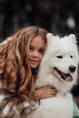 Noel 'i ve yeni yılı kutlayan bayan çocuk kış tatilini dışarıda kutluyor. Küçük kız açık havada beyaz Samoylu köpekle Noel otobüsünün yanında eğleniyor. Çocukluğun tadını çıkarıyor.