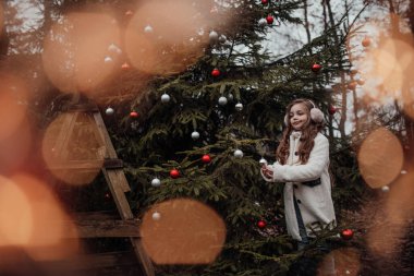 Aktif küçük kız ormanda istirahat edip çocukluk yılbaşı balolarının tadını çıkarıyor. Noel 'i ve yeni yılı kutlayan kadın çocuk kış tatilini dışarıda kutluyor.