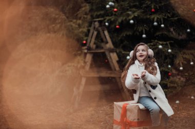 Noel 'i ve yeni yılı kutlayan bayan çocuk kış tatilini dışarıda kutluyor. Aktif küçük kız kozalaklı ormanda çocukluğunun tadını çıkarıyor.