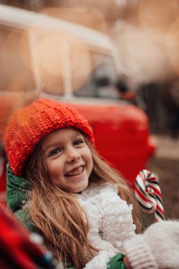 Noel 'i ve yeni yılı kutlayan bayan çocuk kış tatilini dışarıda kutluyor. Kırmızı örgü şapkalı aktif küçük kız elinde Noel şekeri bastonuyla açık havada vakit geçiriyor.