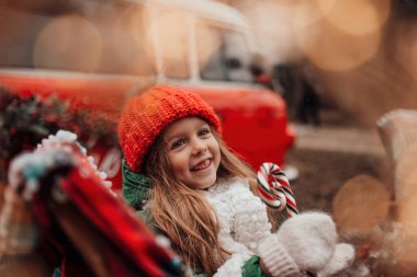 Noel 'i ve yeni yılı kutlayan bayan çocuk kış tatilini dışarıda kutluyor. Kırmızı örgü şapkalı aktif küçük kız elinde Noel şekeri bastonuyla açık havada vakit geçiriyor.