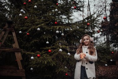 Aktif küçük kız ormanda istirahat edip çocukluk yılbaşı balolarının tadını çıkarıyor. Noel 'i ve yeni yılı kutlayan kadın çocuk kış tatilini dışarıda kutluyor.