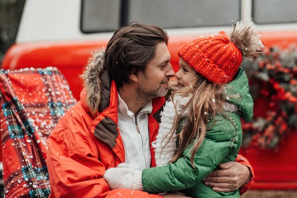Happy family celebrating Christmas and New Year winter holidays season outdoor. Father with little daughter joyful spending time together hugging having fun near Xmas bus rejoices at first snow