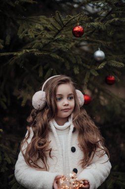 Aktif küçük kız ormanda istirahat edip çocukluk yılbaşı balolarının tadını çıkarıyor. Noel 'i ve yeni yılı kutlayan kadın çocuk kış tatilini dışarıda kutluyor.