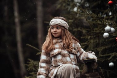 Aktif küçük kız ormanda istirahat edip çocukluk yılbaşı balolarının tadını çıkarıyor. Noel 'i ve yeni yılı kutlayan kadın çocuk kış tatilini dışarıda kutluyor.