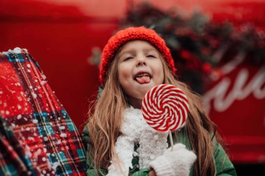 Noel 'i ve yeni yılı kutlayan bayan çocuk kış tatilini dışarıda kutluyor. Kırmızı örgü şapkalı aktif küçük kız elinde Noel şekeri bastonuyla açık havada vakit geçiriyor.