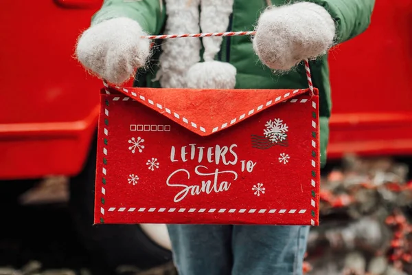 クリスマスと新年の冬休みシーズンの屋外を祝う女性の子供 赤い封筒でサンタに手紙を保持し 奇跡を待っているオープンエアで楽しい時間を過ごす少女 — ストック写真