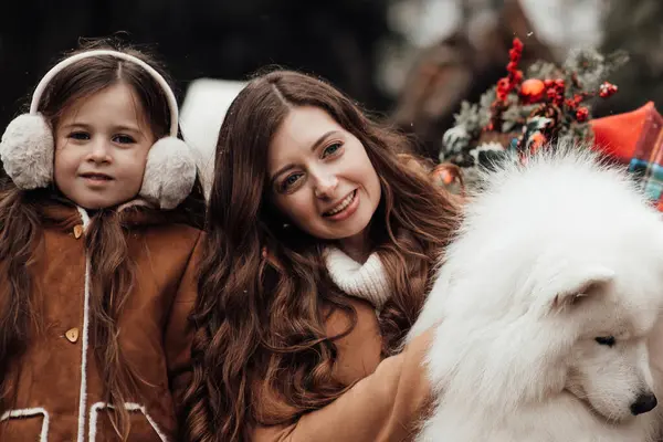 全家在户外欢度圣诞和新年佳节 与母亲和白种萨摩亚狗的女儿欢欢喜喜地在圣诞大巴附近拥抱 — 图库照片