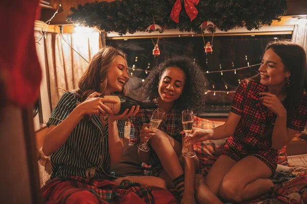 キャンパーでクリスマスと新年の冬の休暇シーズンを祝うハッピーガールズ アクティブな若い多様な女性が一緒に抱擁する楽しい時間を過ごし 古いXmasトレーラーでスパークリングワインを飲む楽しみを持っています — ストック写真
