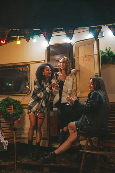 快乐的女孩们在户外庆祝圣诞节和新年假期 年轻而多样化的女性快乐的女性朋友在旧式的圣诞预告片旁畅饮起泡的美酒 — 图库照片
