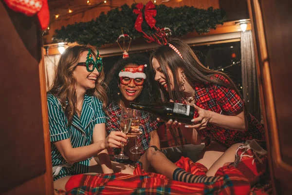 快乐的女孩们在营地庆祝圣诞节和新年假期 活跃的 多样化的年轻女性快乐地拥抱在一起 在旧式的圣诞预告片里畅饮起泡的葡萄酒 — 图库照片