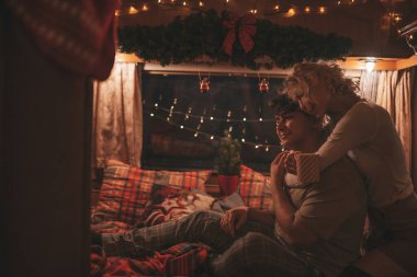 Noel 'i ve yeni yılı kutlayan mutlu çift kış tatili sezonunu karavanda kutluyor. Çay içen genç çift Xmas karavanında sarılıp öpüşüyor.