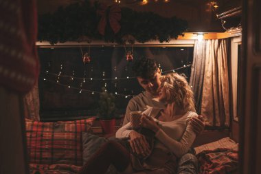 Noel 'i ve yeni yılı kutlayan mutlu çift kış tatili sezonunu karavanda kutluyor. Çay içen genç çift Xmas karavanında sarılıp öpüşüyor.