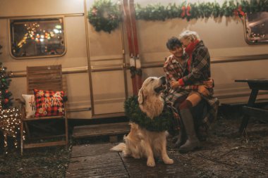 Noel 'i ve yeni yılı kutlayan mutlu çift, kış tatili sezonunu Camper Park' ta kutluyor. Genç mutlu çift, Xmas karavanı yakınında Golden Retriever köpeğiyle sarılıp vakit geçiriyorlar.