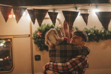 Noel 'i ve yeni yılı kutlayan mutlu çift, kış tatili sezonunu Camper Park' ta kutluyor. Genç çift dinleniyor ve rahatlıyor. Birlikte zaman geçiriyorlar. Xmas karavanı yakınında sarılıp öpüşüyorlar.