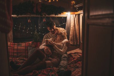 Noel 'i ve yeni yılı kutlayan mutlu çift kış tatili sezonunu karavanda kutluyor. Çay içen genç çift Xmas karavanında sarılıp öpüşüyor.