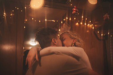 Noel 'i ve yeni yılı kutlayan mutlu çift kış tatili sezonunu karavanda kutluyor. Çay içen genç çift Xmas karavanında sarılıp öpüşüyor.