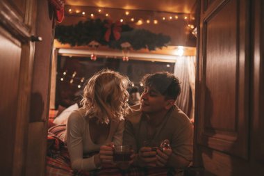 Noel 'i ve yeni yılı kutlayan mutlu çift kış tatili sezonunu karavanda kutluyor. Çay içen genç çift Xmas karavanında sarılıp öpüşüyor.