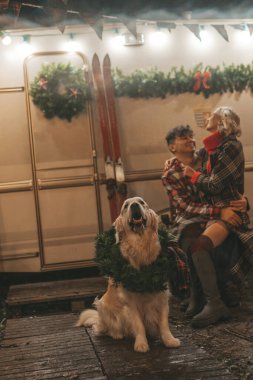 Noel 'i ve yeni yılı kutlayan mutlu çift, kış tatili sezonunu Camper Park' ta kutluyor. Genç mutlu çift, Xmas karavanı yakınında Golden Retriever köpeğiyle sarılıp vakit geçiriyorlar.