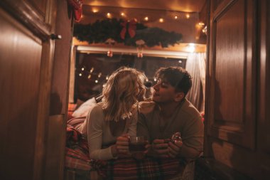 Noel 'i ve yeni yılı kutlayan mutlu çift kış tatili sezonunu karavanda kutluyor. Çay içen genç çift Xmas karavanında sarılıp öpüşüyor.